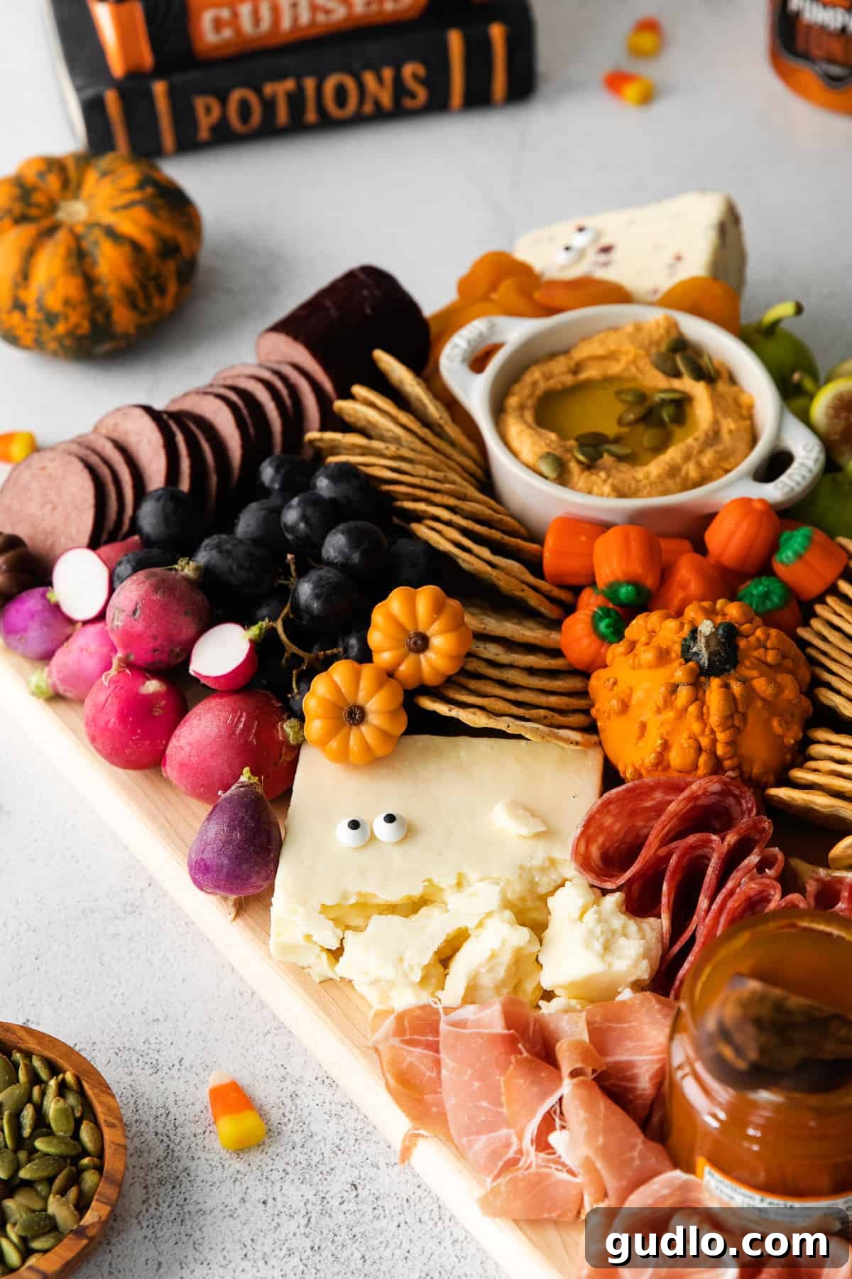 Ghoulish Grazing Board 6 A vibrant Halloween cheese board filled with various snacks, including cheese, crackers, fruits, olives, and candy eyes.