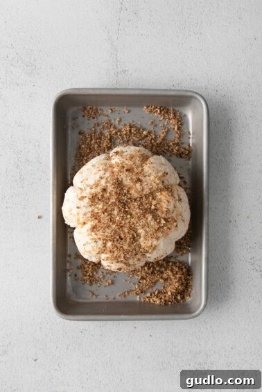 A pumpkin cheese ball being rolled in a bowl of finely chopped pecans.