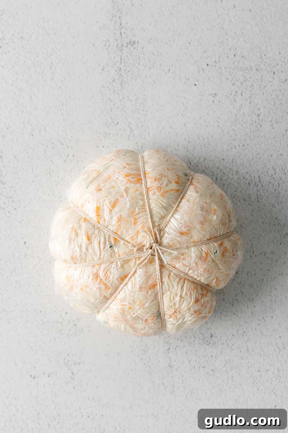 The Art of Shaping Your Pumpkin Cheese Ball A partially shaped cheese ball with kitchen twine tied around it, creating pumpkin segments.