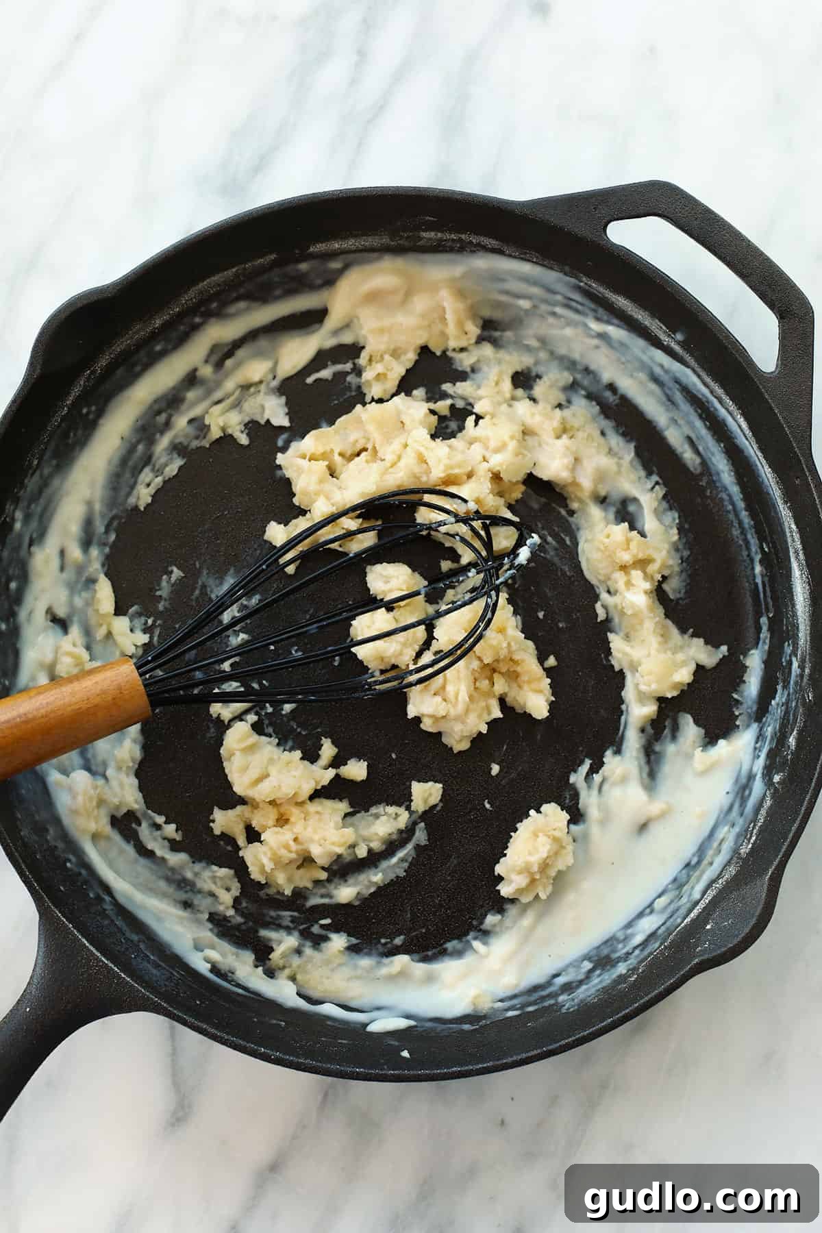 Beginning the delicious cheese sauce with a perfectly made roux. Cast iron skillet with a whisk in it whisking together a roux for the mac and cheese sauce.