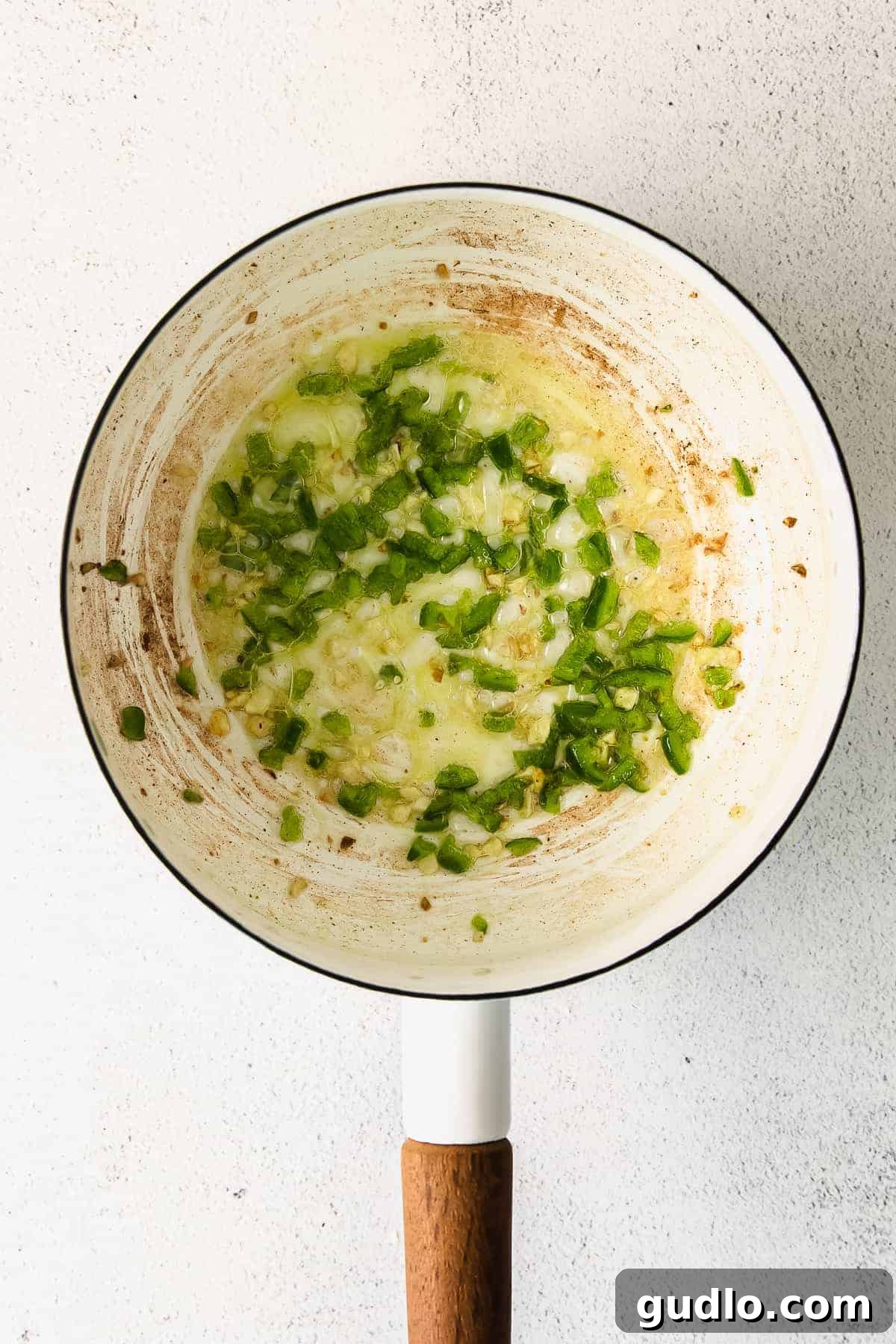 Sautéing Aromatics for Queso Dip Freshly chopped onions and jalapeños being sautéed in a pot, forming the flavorful base of homemade queso dip.