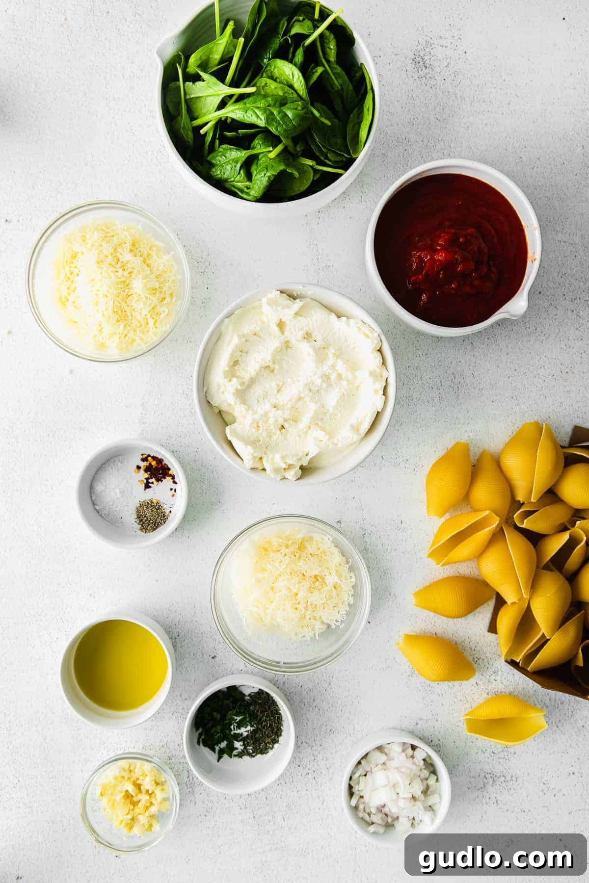 Fresh Ingredients Ready for Ricotta Stuffed Shells Preparation A collection of fresh ingredients for ricotta stuffed shells, including jumbo shells, cheeses, herbs, and aromatics, neatly arranged in small bowls.