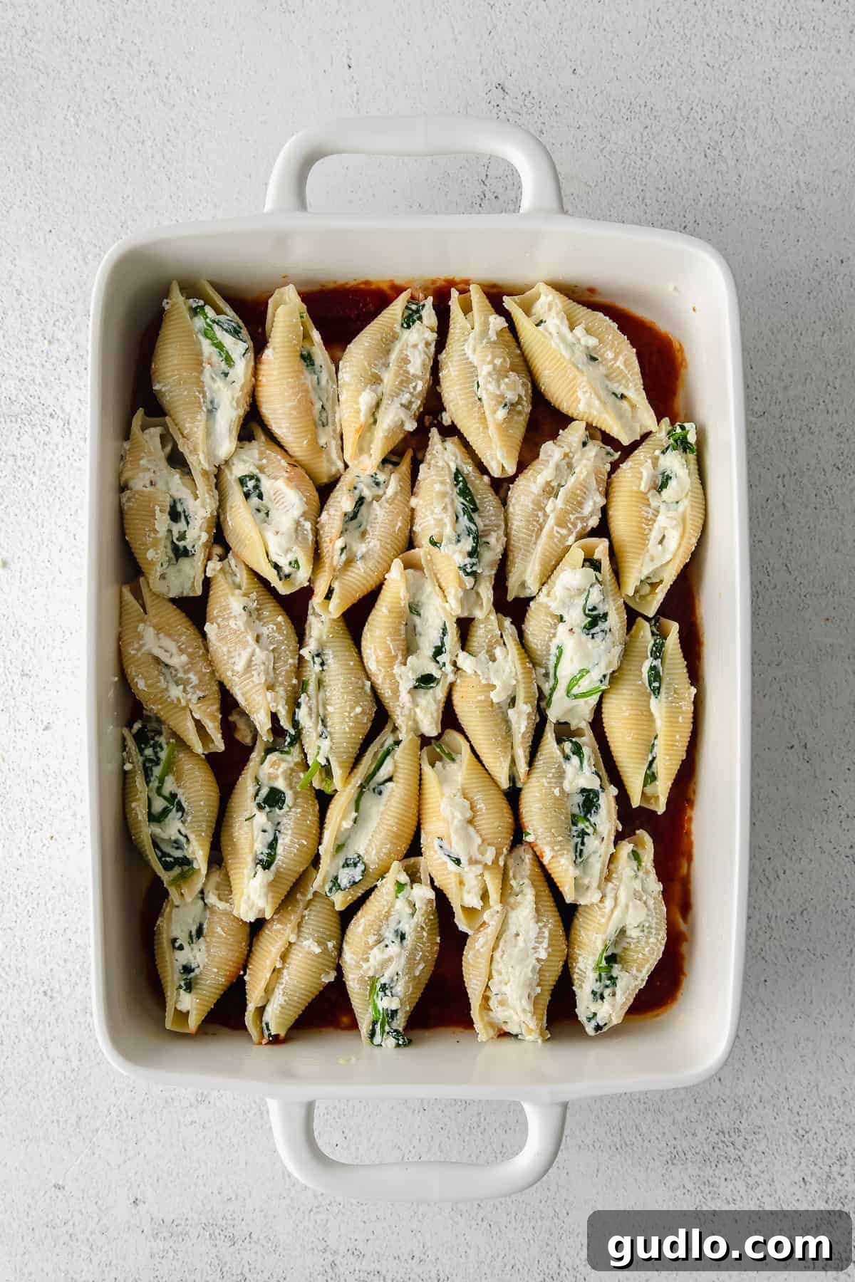 Assembled Stuffed Shells in Baking Dish Before Cooking Unbaked ricotta stuffed shells neatly arranged in a casserole dish, covered with marinara sauce and ready for the oven.