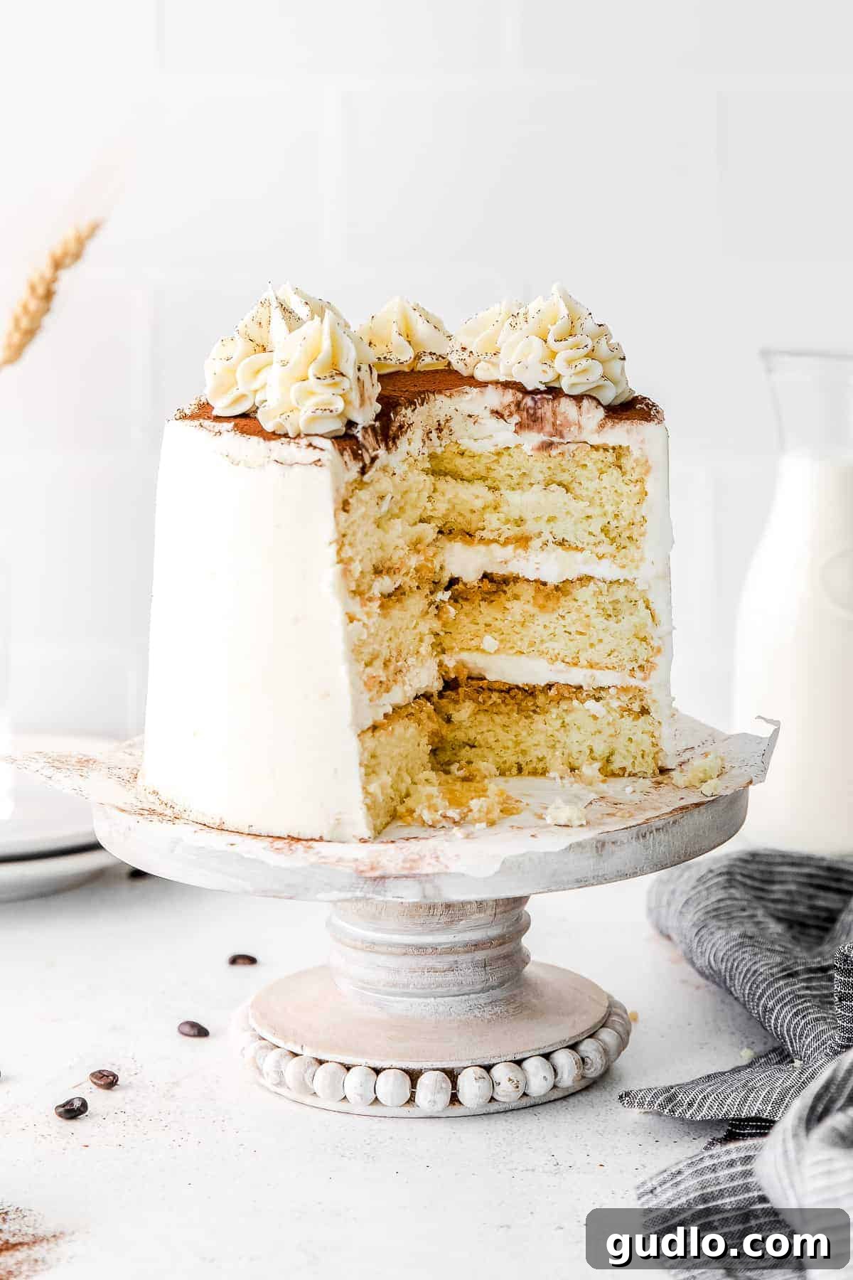 A beautifully presented Tiramisu Layer Cake with a slice gracefully removed, revealing the espresso-soaked layers and creamy mascarpone filling.
