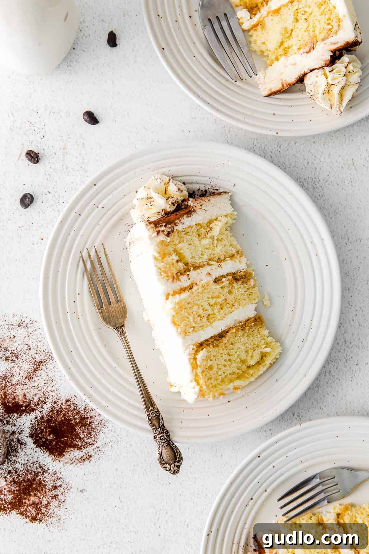 A perfect slice of Tiramisu Layer Cake beautifully presented on a plate with a fork, ready to be enjoyed.