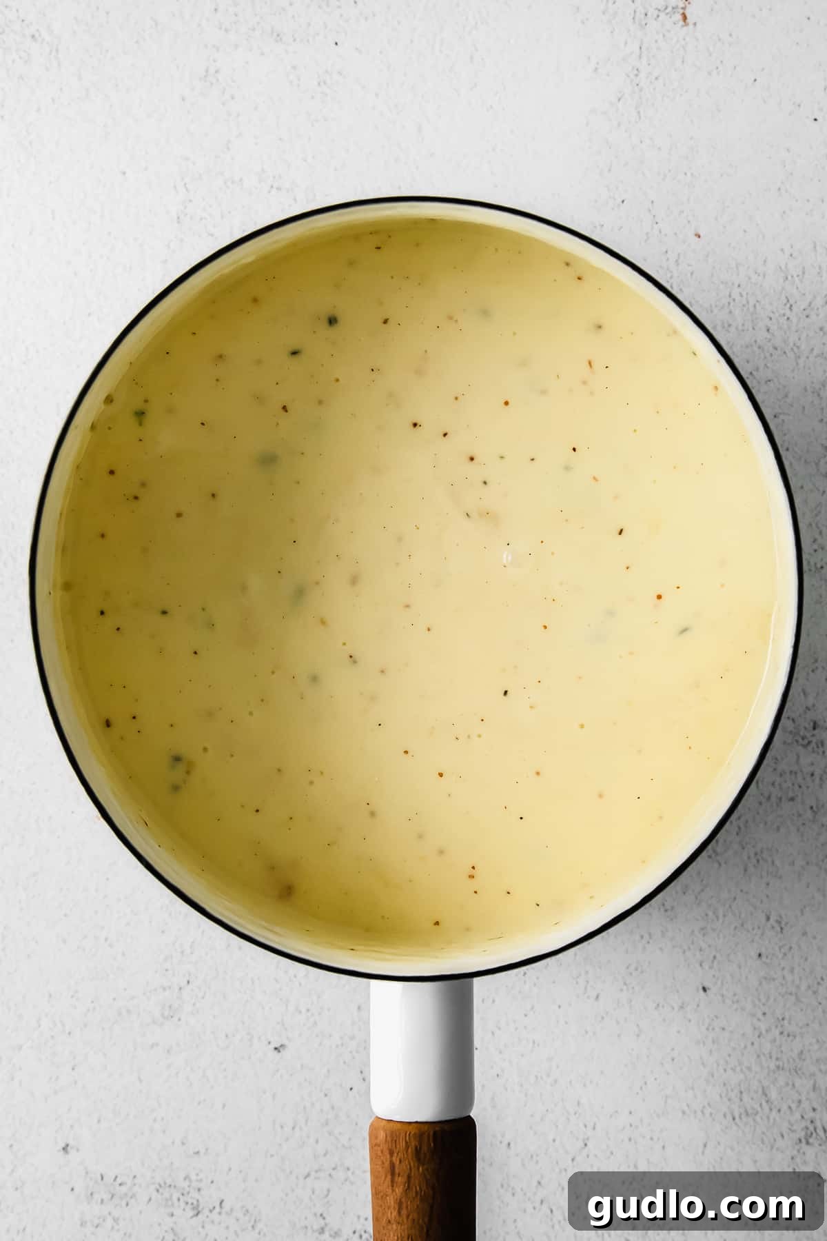 Smooth and creamy cheese fondue simmering gently in a saucepan, ready to be transferred to a fondue pot.