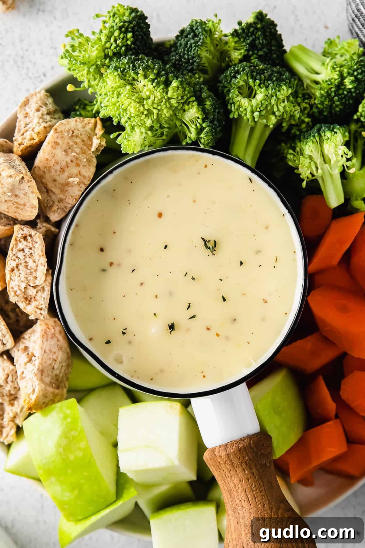 A fondue pot filled with rich cheese fondue, surrounded by an appetizing array of vegetables and bread cubes.