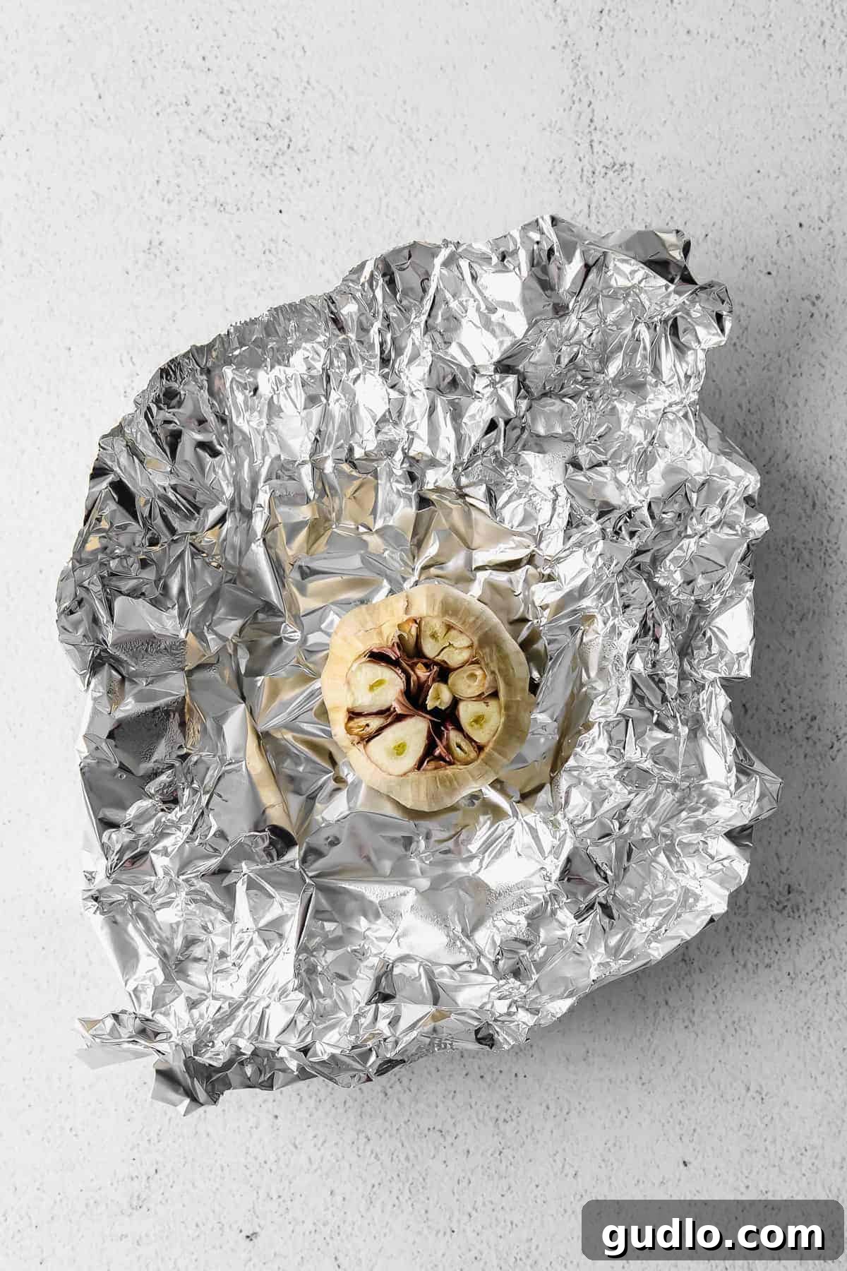 A head of garlic wrapped in aluminum foil, ready for roasting