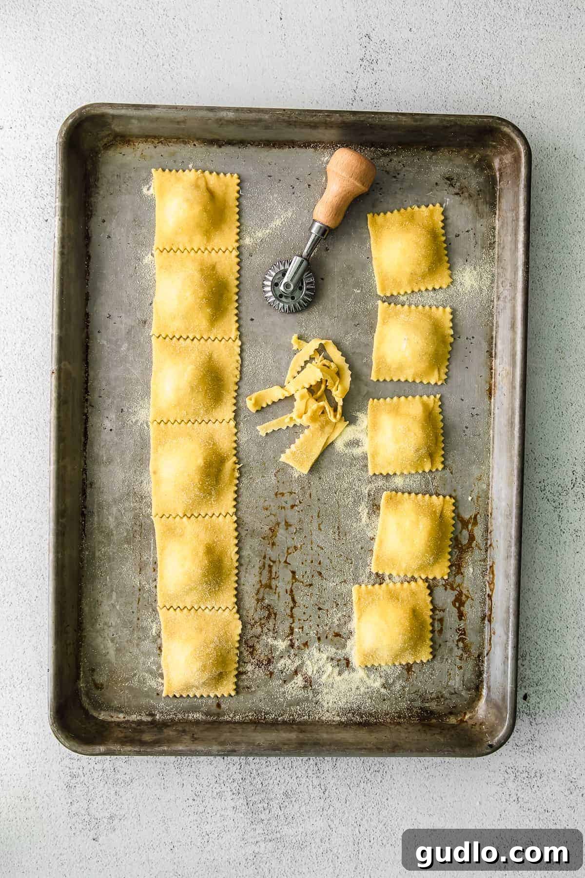 Homemade cheese ravioli being cut with a pasta wheel on a baking sheet.