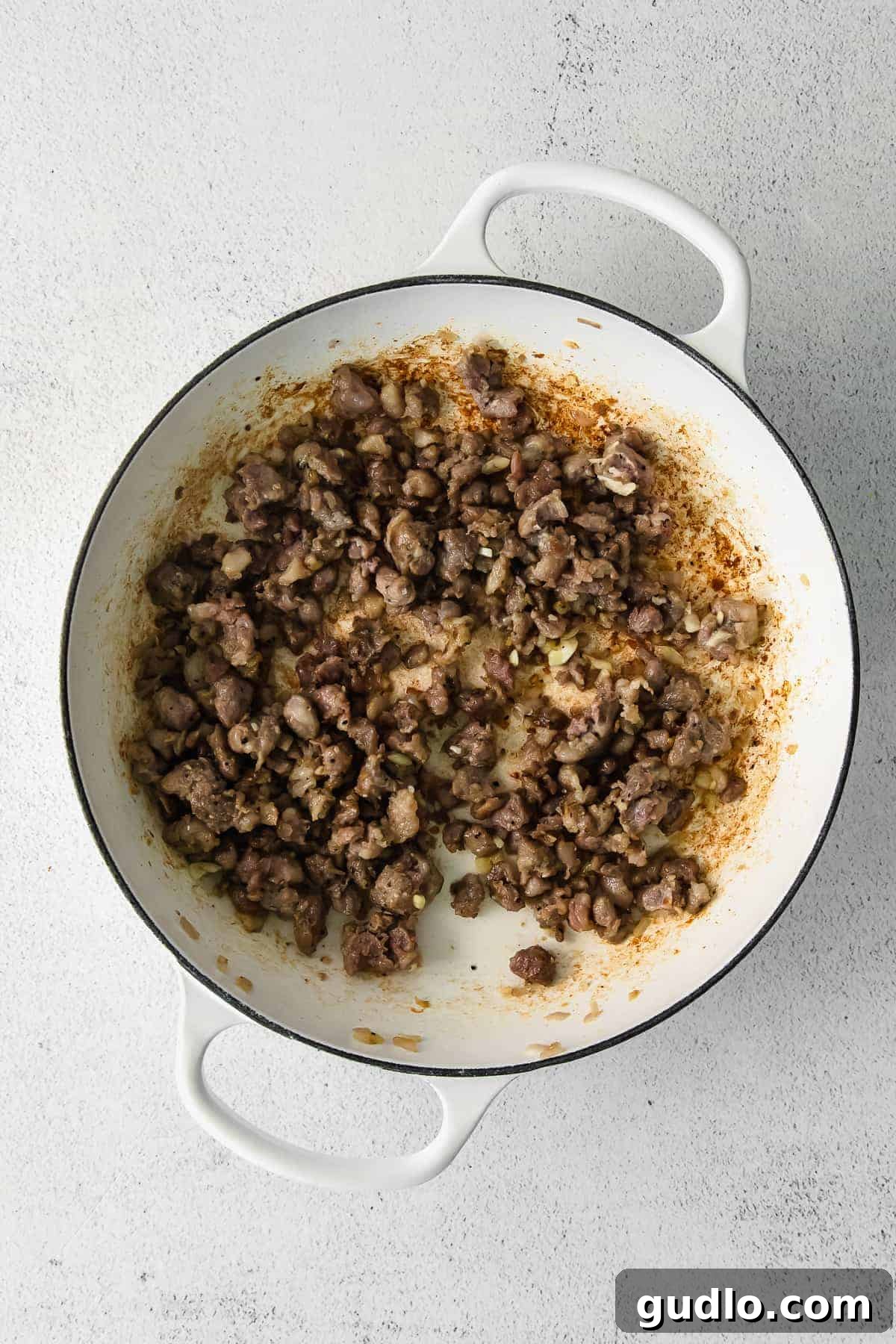 Crumbled and browned Italian sausage cooking in a skillet, releasing savory aromas.