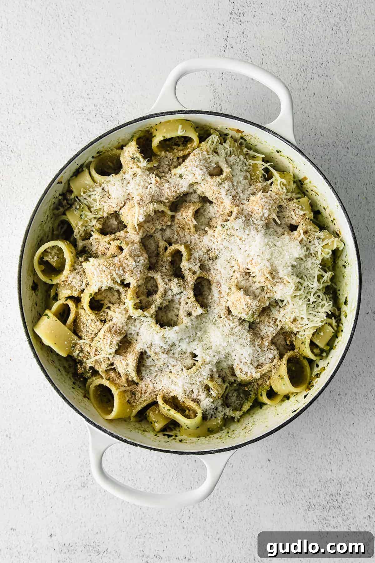 A close-up shot of cooked pesto pasta with melted cheese and crispy breadcrumb topping in a large skillet.