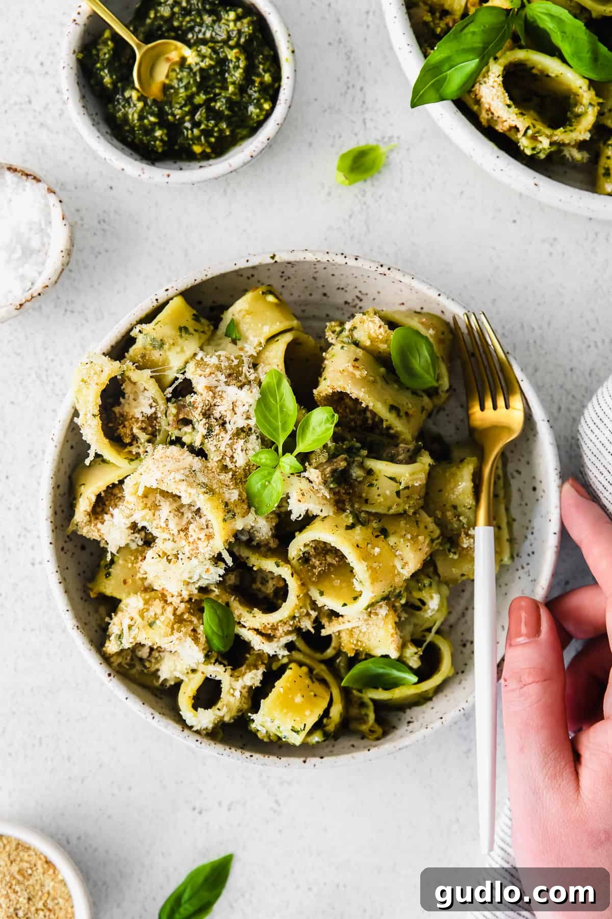 A bowl of creamy pesto pasta with Italian sausage, topped with fresh basil and Parmesan cheese, ready to be enjoyed.