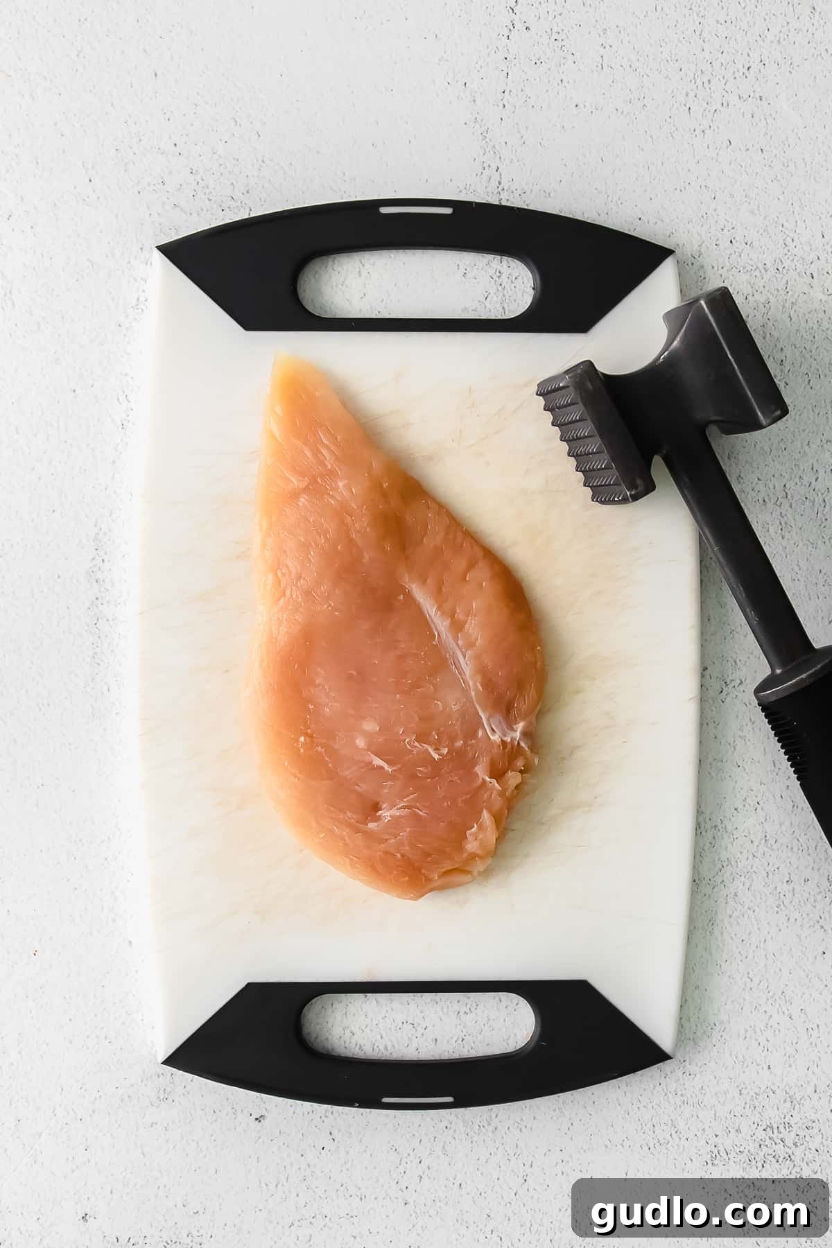 Tenderizing Chicken Breasts for Cordon Bleu chicken breast on a cutting board with a tenderizing mallet