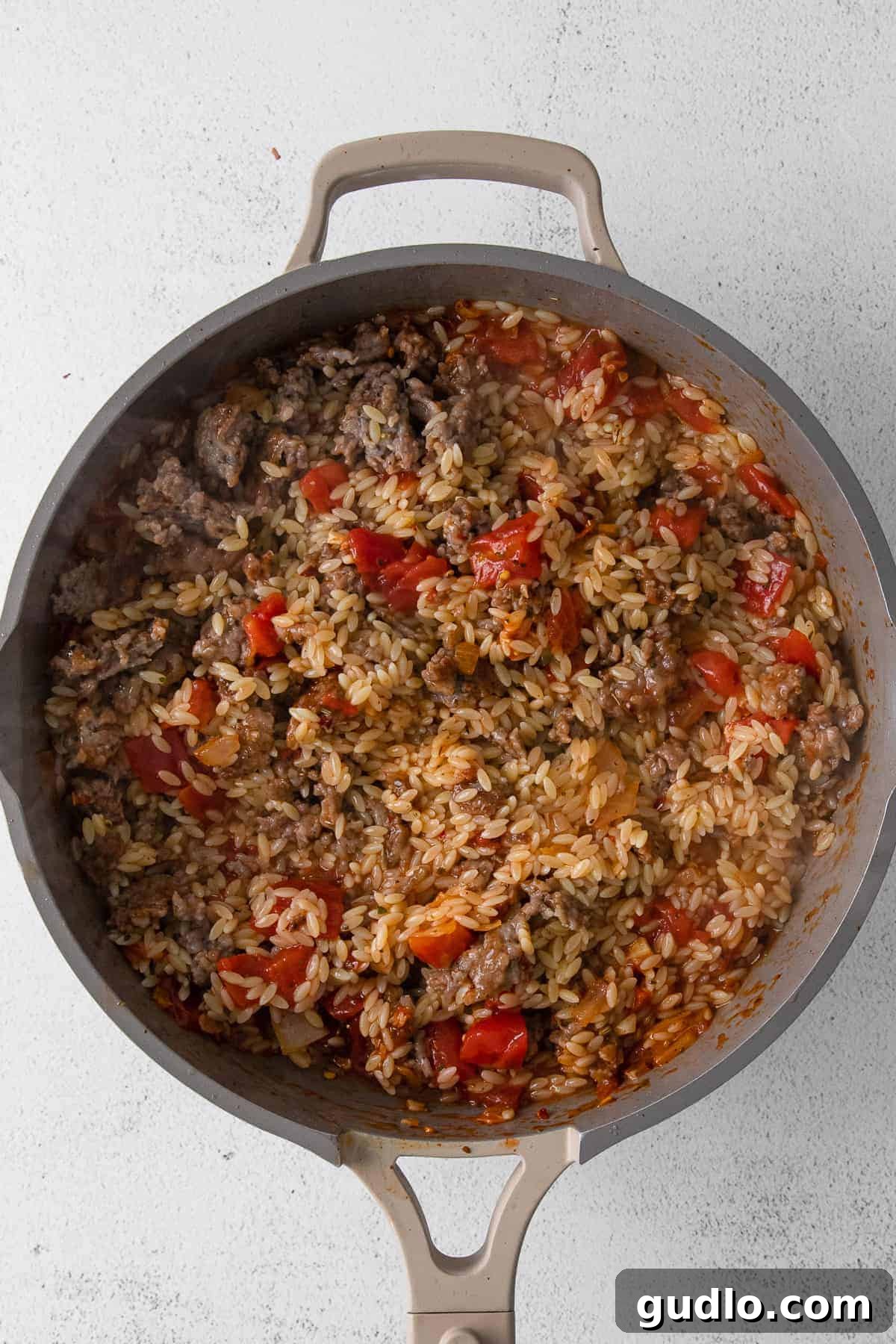 Rich and savory orzo and sausage filling mixed in a pan, ready to be stuffed into bell peppers.