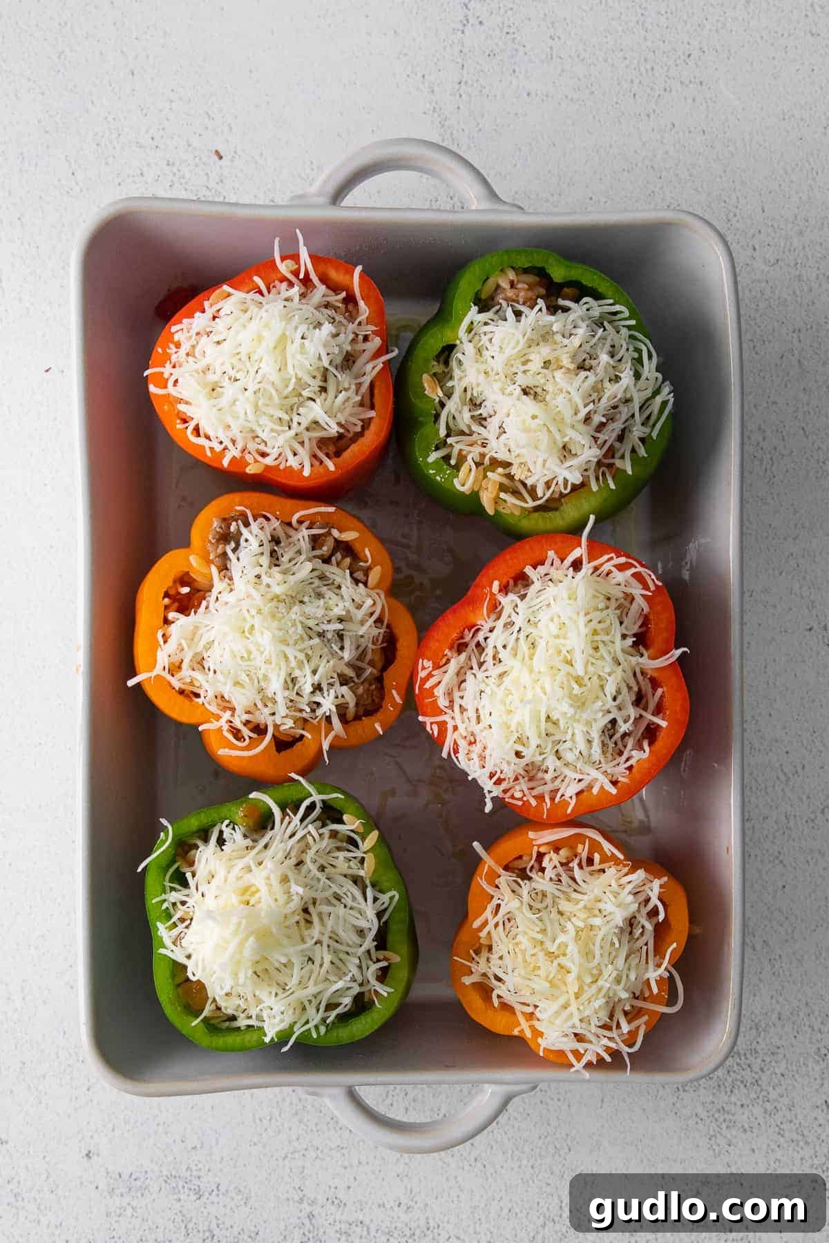 Bell peppers generously topped with shredded mozzarella and Parmesan cheese, ready for baking to golden perfection.