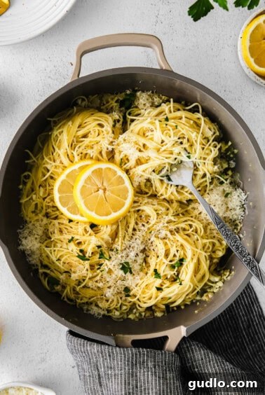 A beautifully garnished pan of lemon garlic pasta, ready to be served, with lemon slices and Parmesan cheese.