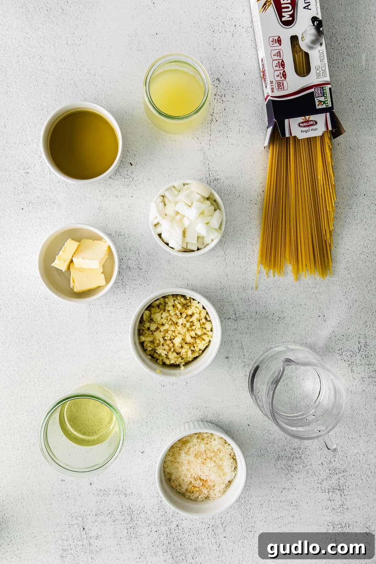 A collection of fresh ingredients for lemon garlic pasta laid out on a kitchen countertop, including lemons, garlic, olive oil, and spaghetti.