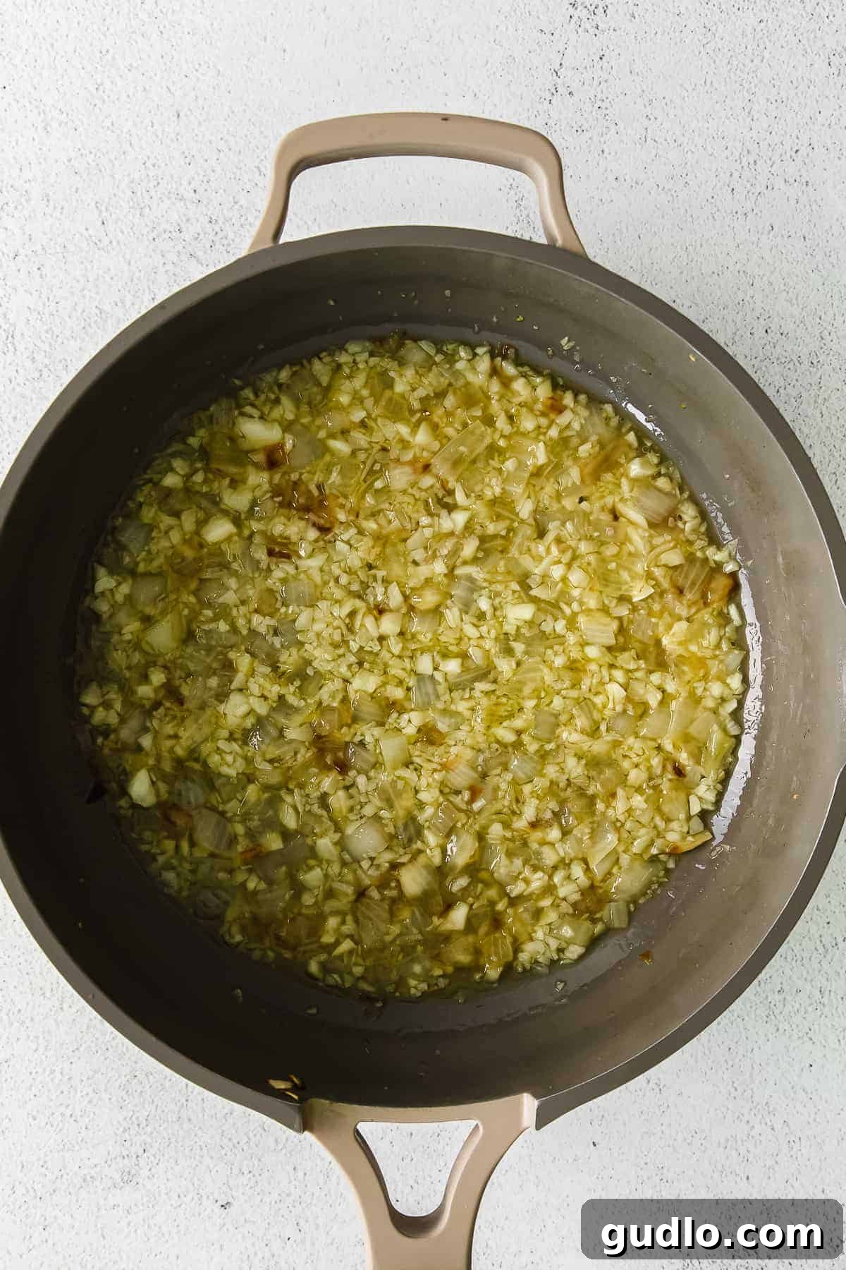 Close-up of lemon garlic pasta sauce simmering in a frying pan, showing onions and garlic.