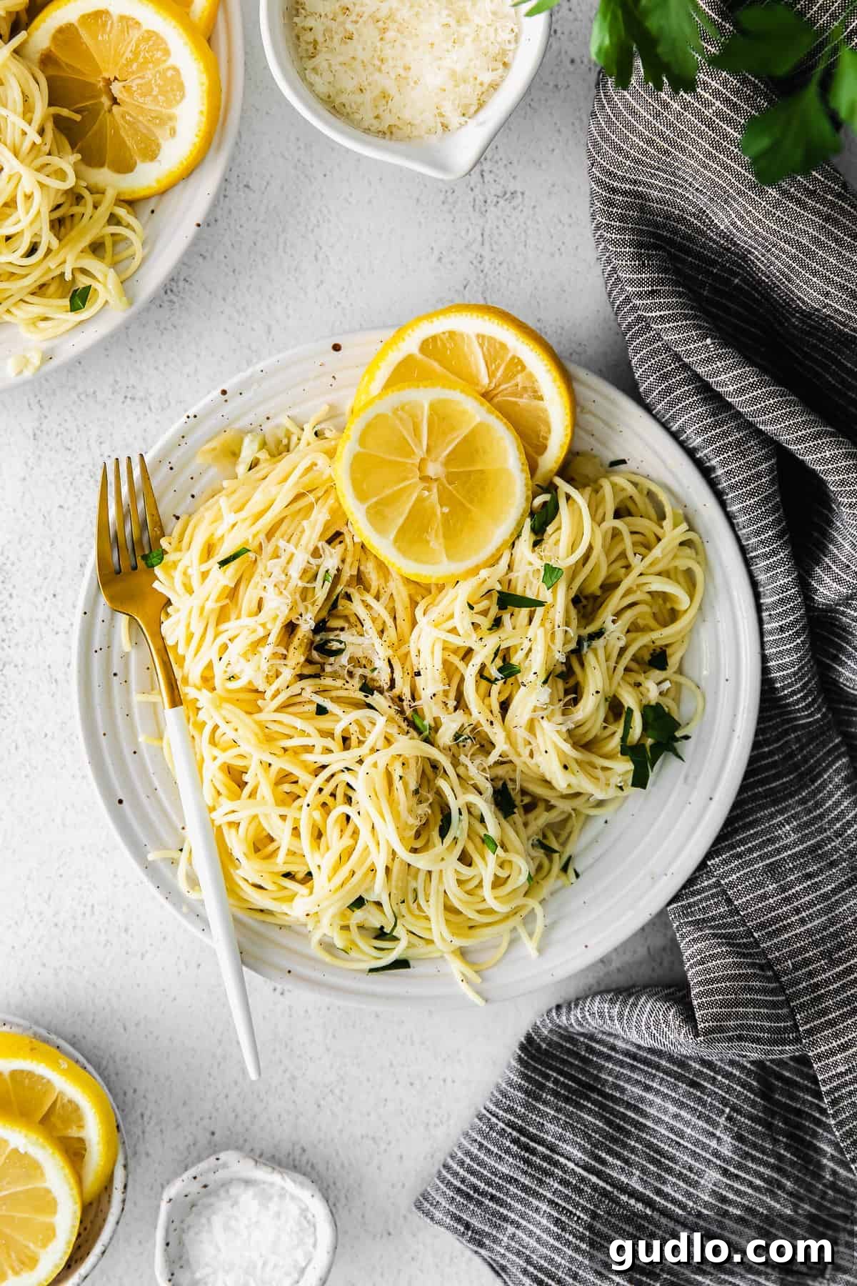 A serving of lemon garlic pasta on a white plate, garnished with parsley and lemon.