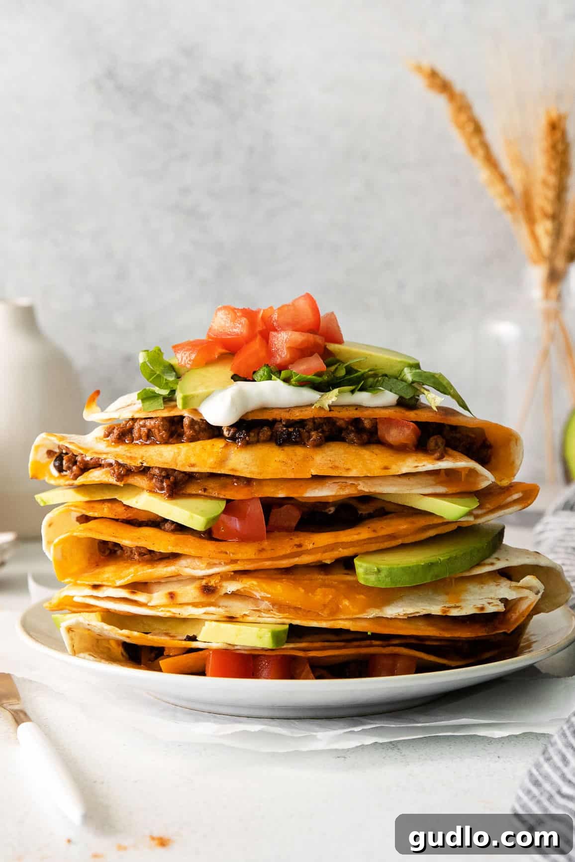 Stack of crispy, golden-brown ground beef quesadillas, garnished with fresh cilantro and lime wedges, ready to be served on a rustic wooden board.