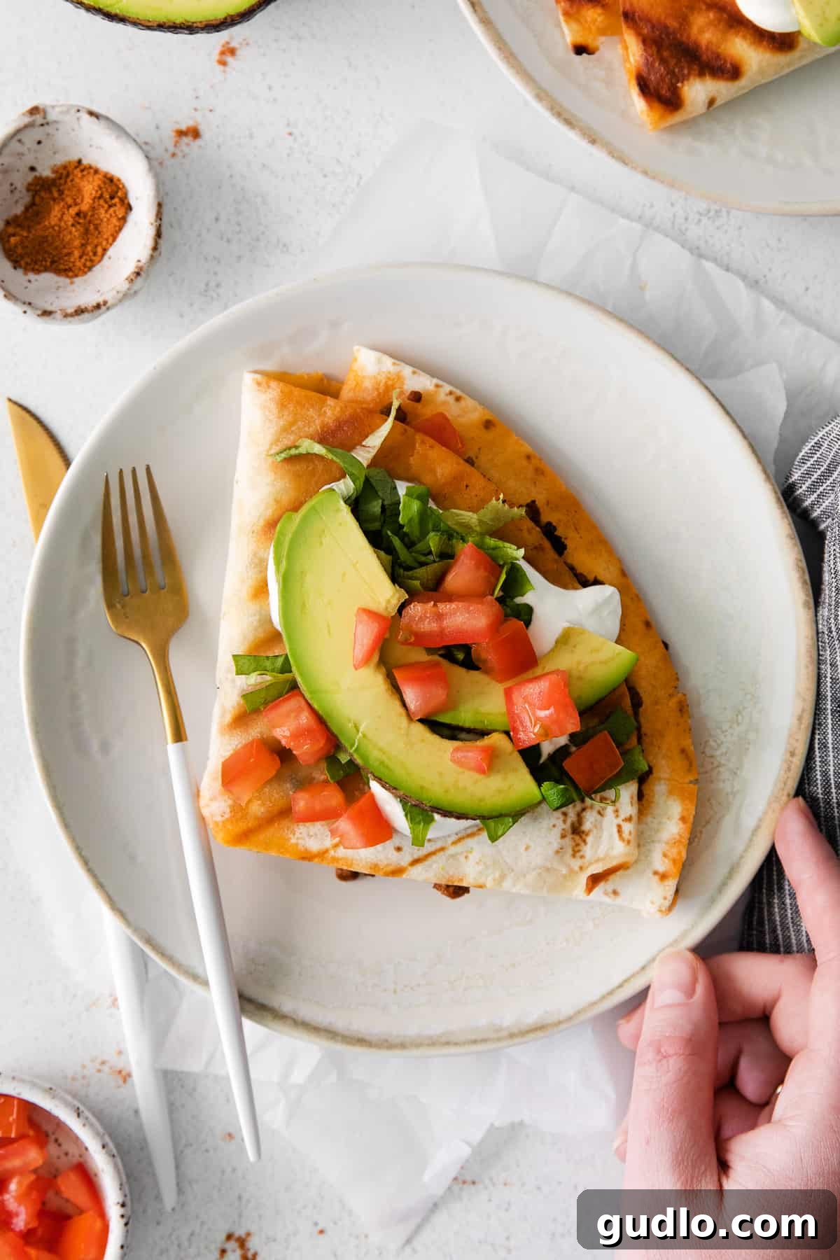 A single, perfectly cooked ground beef quesadilla, cut into neat triangles, artfully presented on a clean white plate with a side of sour cream, fresh cilantro, and a lime wedge.
