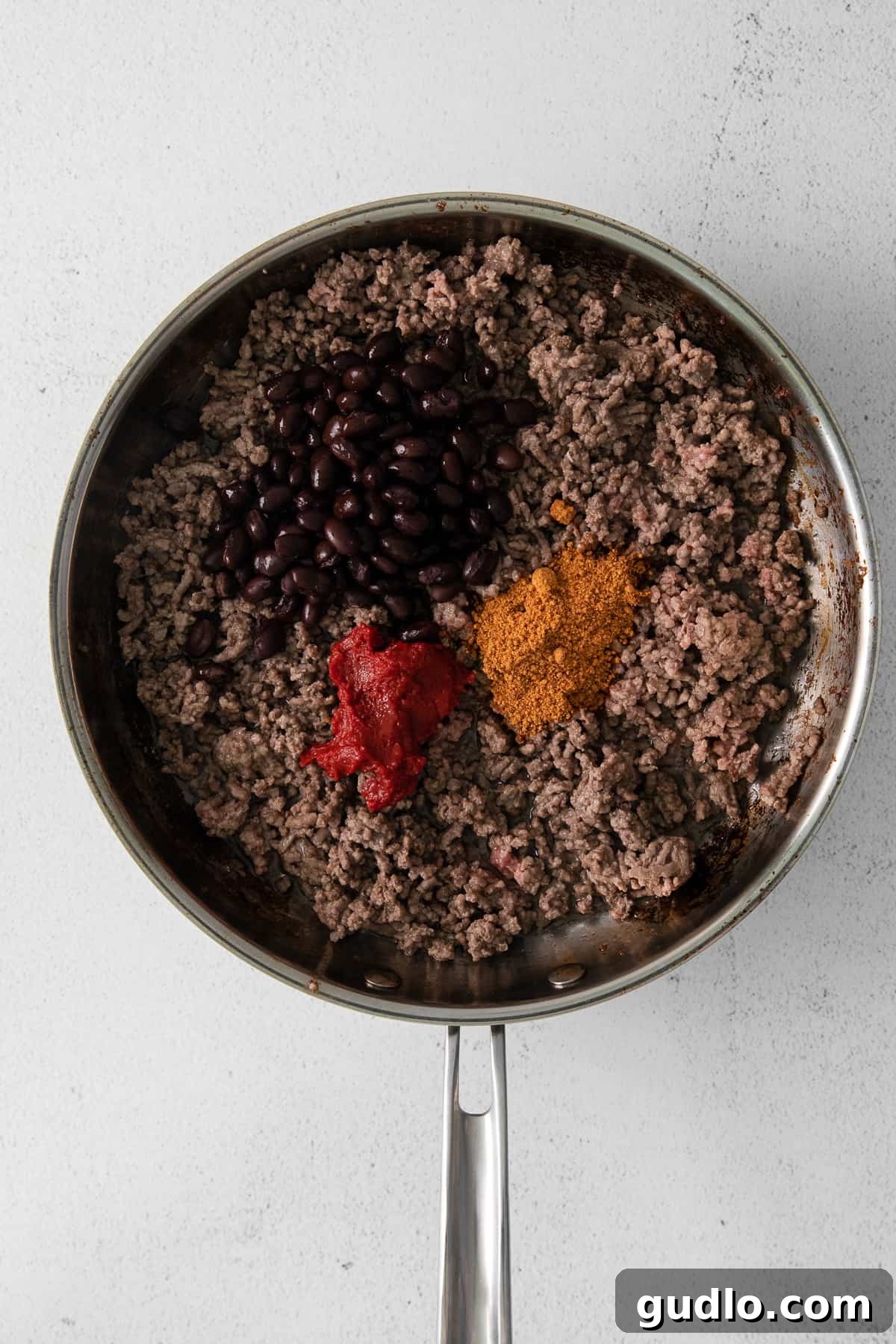 Close-up of browned ground beef simmering with aromatic taco seasoning, rich tomato paste, and dark black beans in a well-seasoned cast iron skillet, creating a flavorful filling.