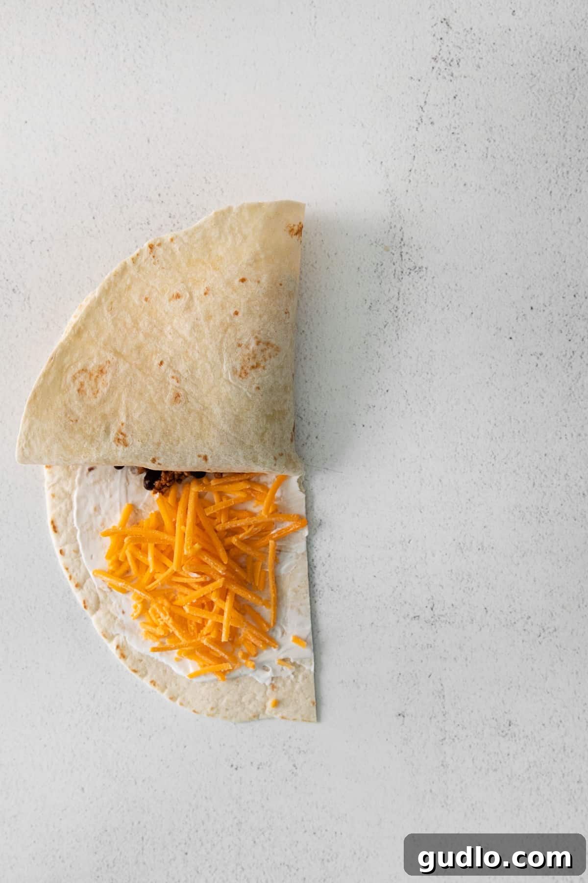 Detailed demonstration of the quadrant folding technique for a quesadilla, showing the precise first fold of the bottom-right section upwards, ensuring ingredients are neatly enclosed.