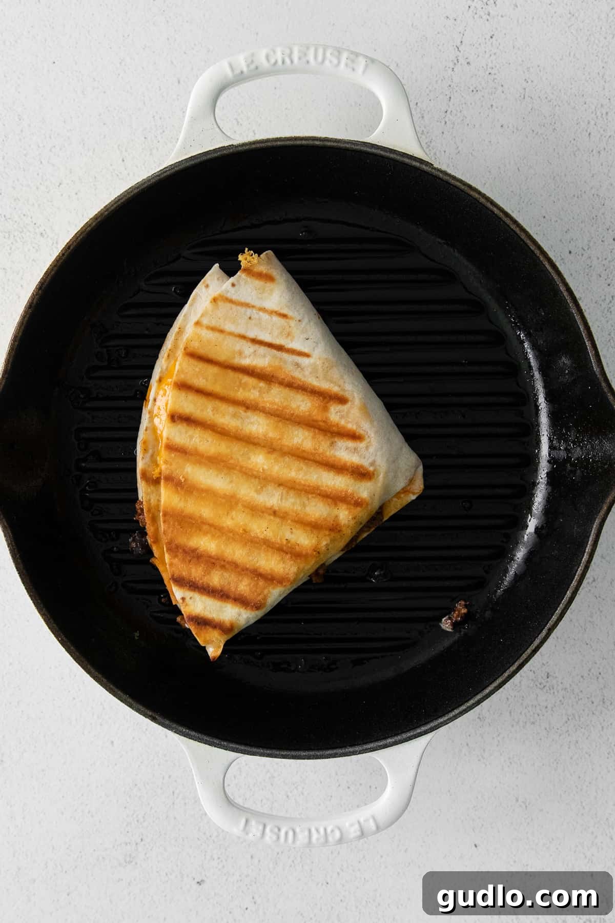 A freshly grilled ground beef quesadilla, perfectly golden and crispy with visible char marks from the grill pan, sizzling gently in the pan.