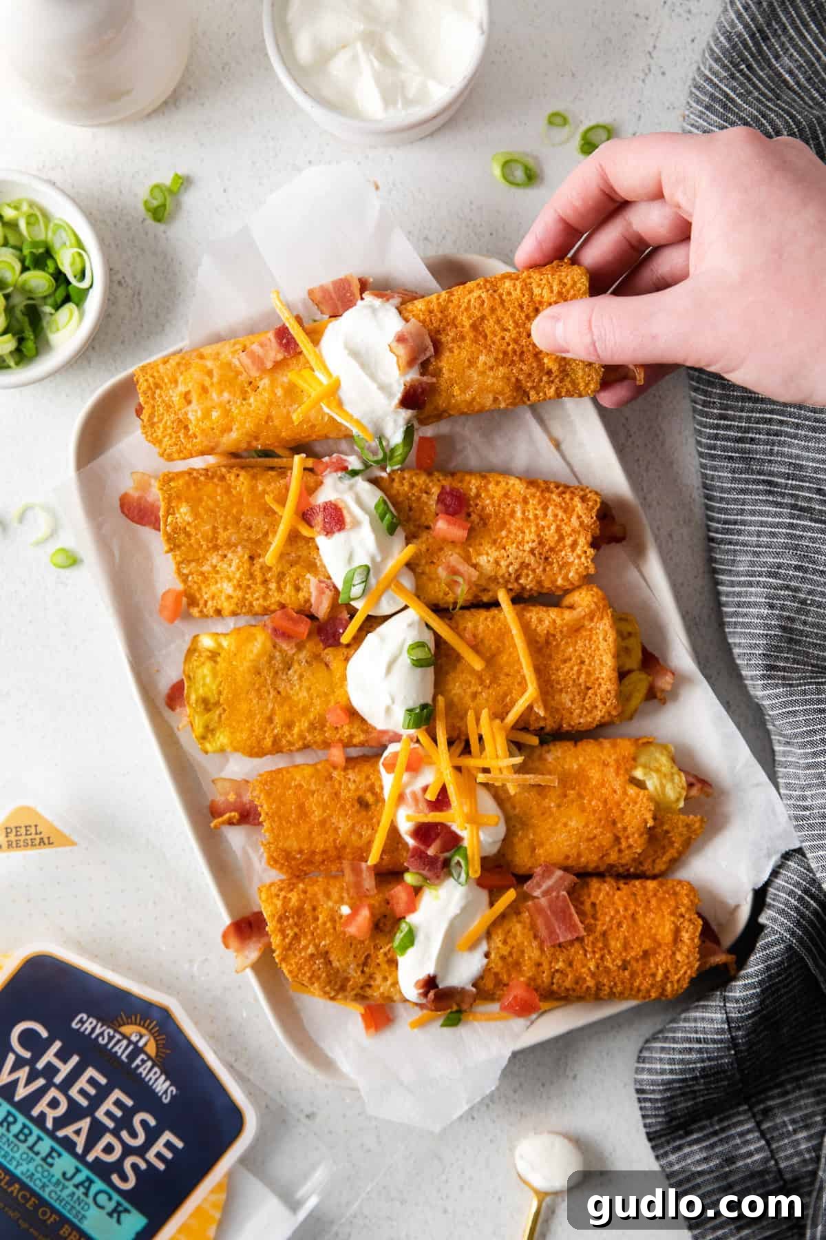 Delicious Eggs and Bacon Breakfast Taquitos in Crispy Cheese Wraps Crispy bacon and egg breakfast taquitos on a plate, garnished with a dollop of sour cream and fresh chives, ready to be enjoyed.