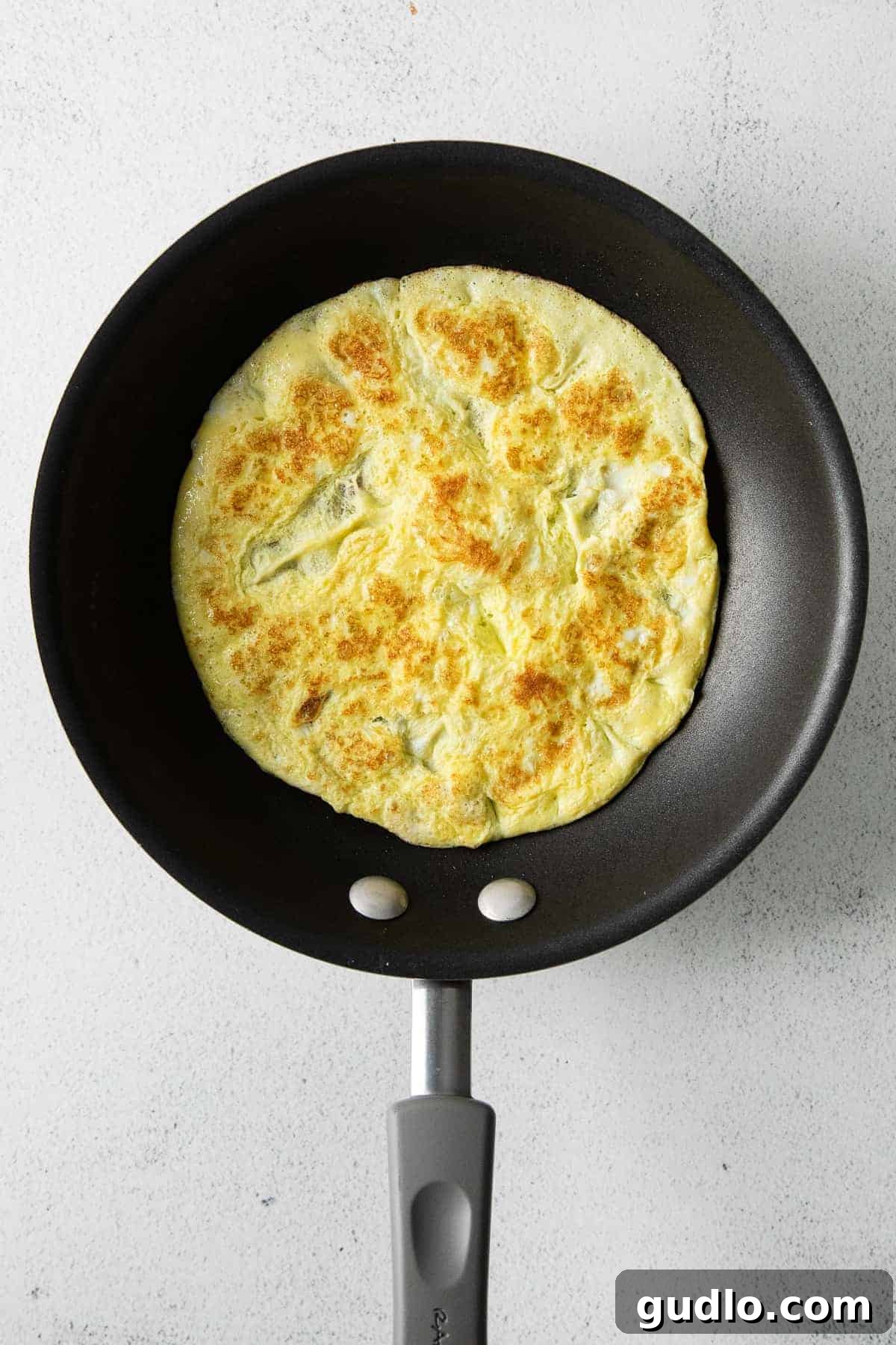 Cooking the Egg Round for Breakfast Taquitos A close-up shot of a single egg cooking in a non-stick skillet, forming a perfect, uniform round, indicating it's ready for flipping.