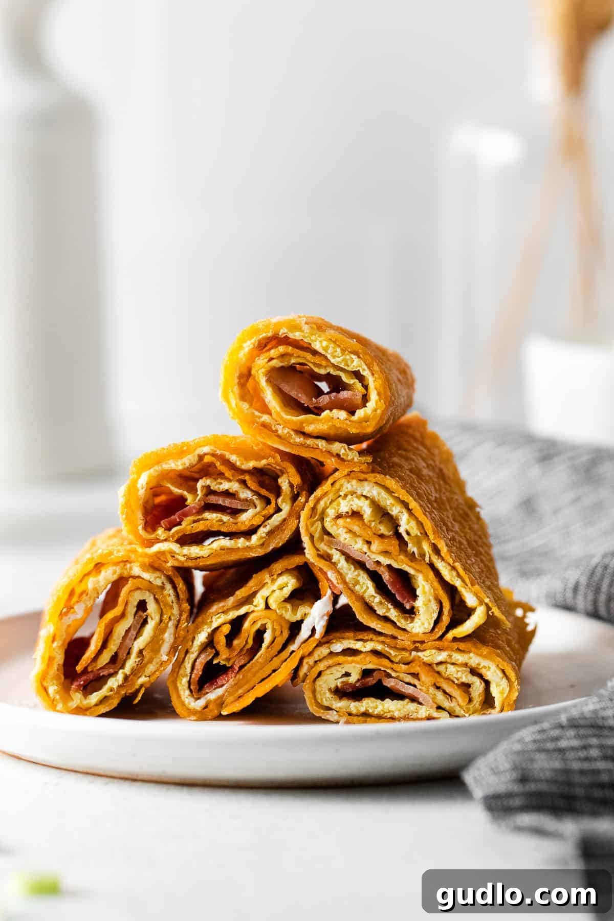 Stacked Crispy Cheese Wrap Breakfast Taquitos with Toppings Several perfectly cooked and golden breakfast taquitos expertly stacked on a white plate, showcasing their delicious crispness and inviting presentation, ready for toppings.