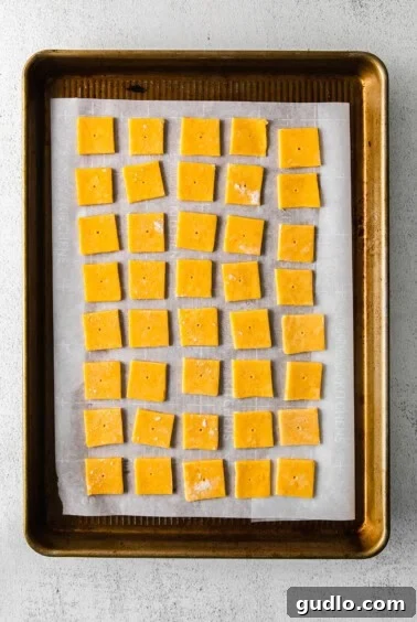 Homemade Golden Cheese Crackers 5 Squares of cheese cracker dough on a baking sheet, with small holes poked in the center of each.