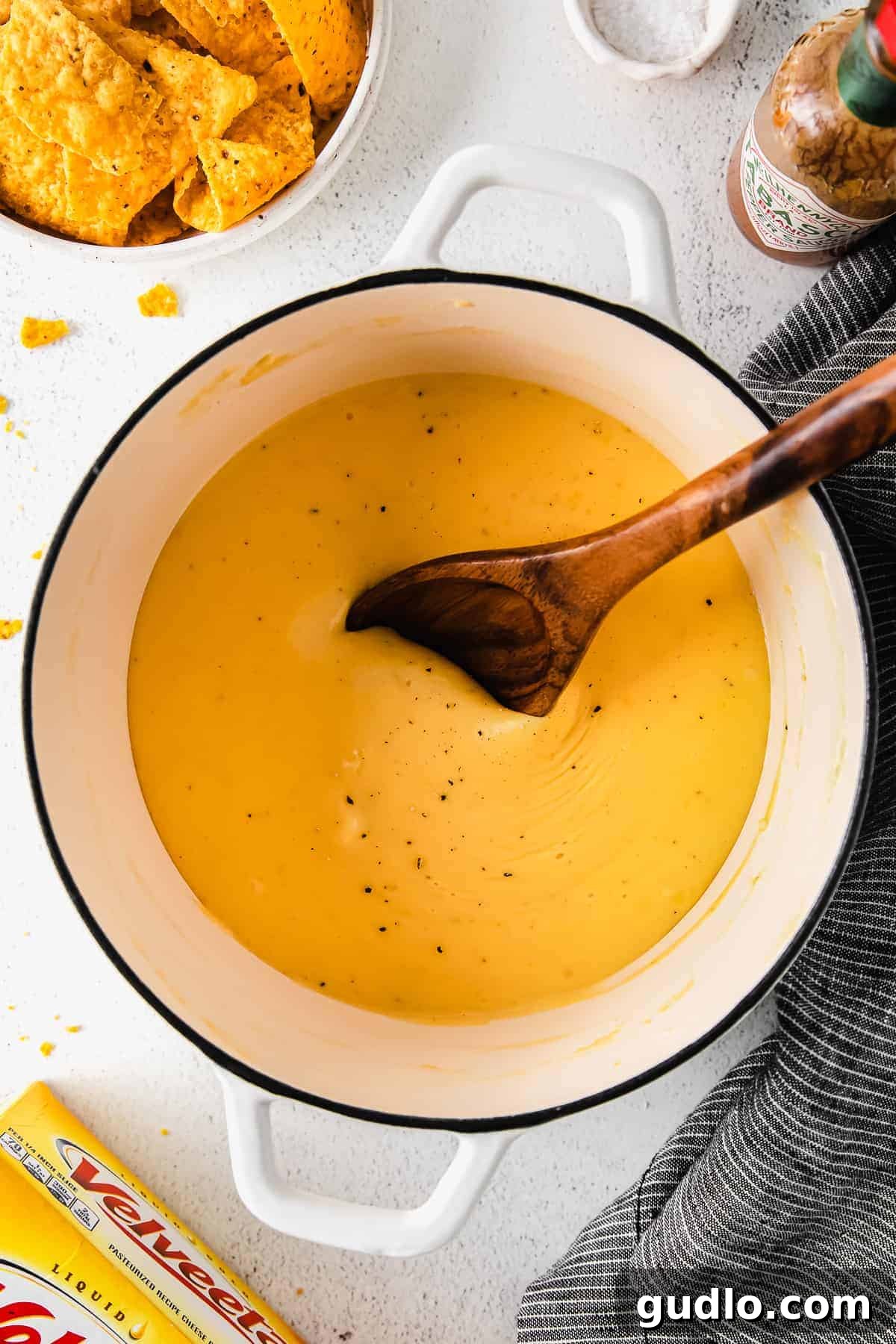 Our Ultimate Velveeta Cheese Sauce is oh so creamy and flavorful and made with easy ingredients. Pair with your favorite pasta, and enjoy! Velveeta cheese sauce simmering in a stock pot with a wooden spoon for serving
