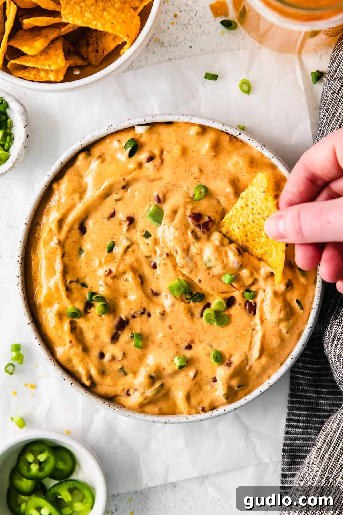 A vibrant bowl of creamy chili cheese dip, generously garnished with fresh green onions, with crispy tortilla chips positioned around it, ready for dipping.