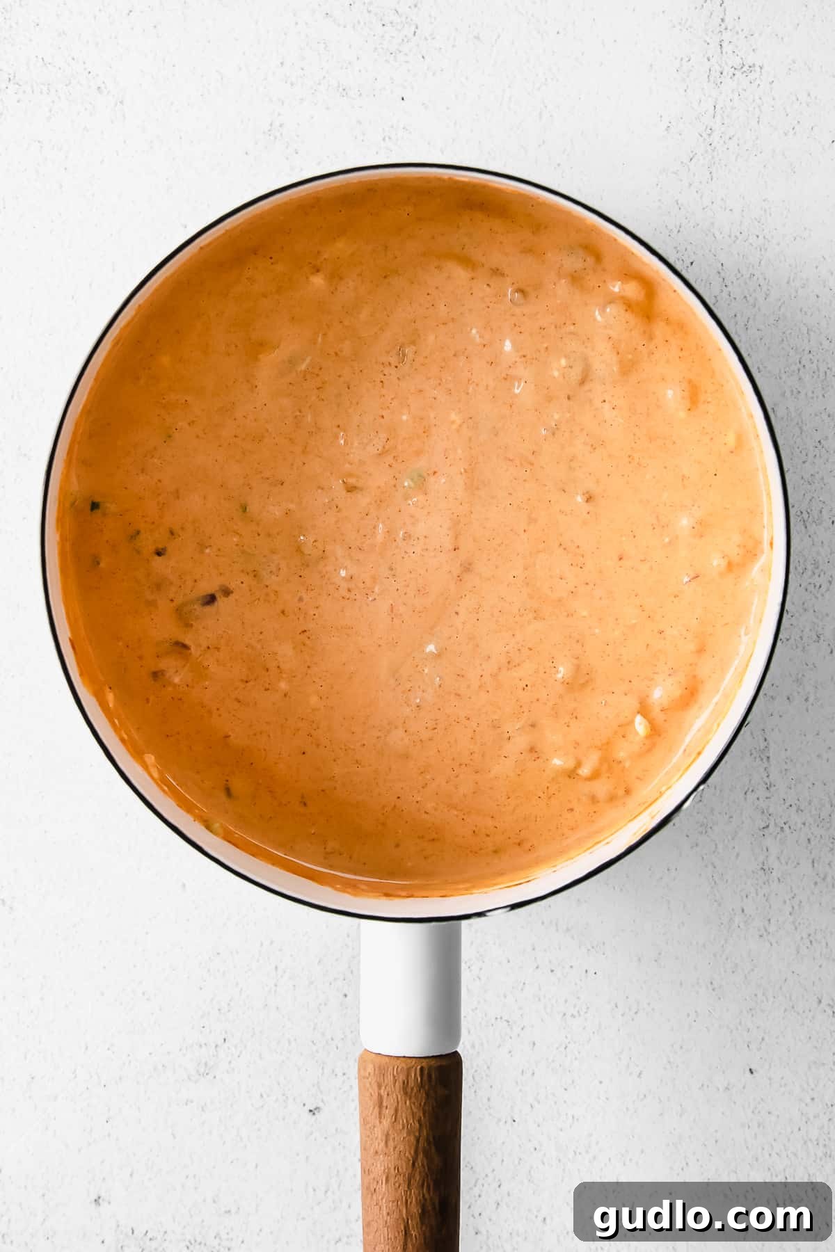 Chili cheese dip melting and bubbling gently in a stainless steel saucepan on the stovetop, showcasing its creamy, molten texture before being transferred to a serving dish.