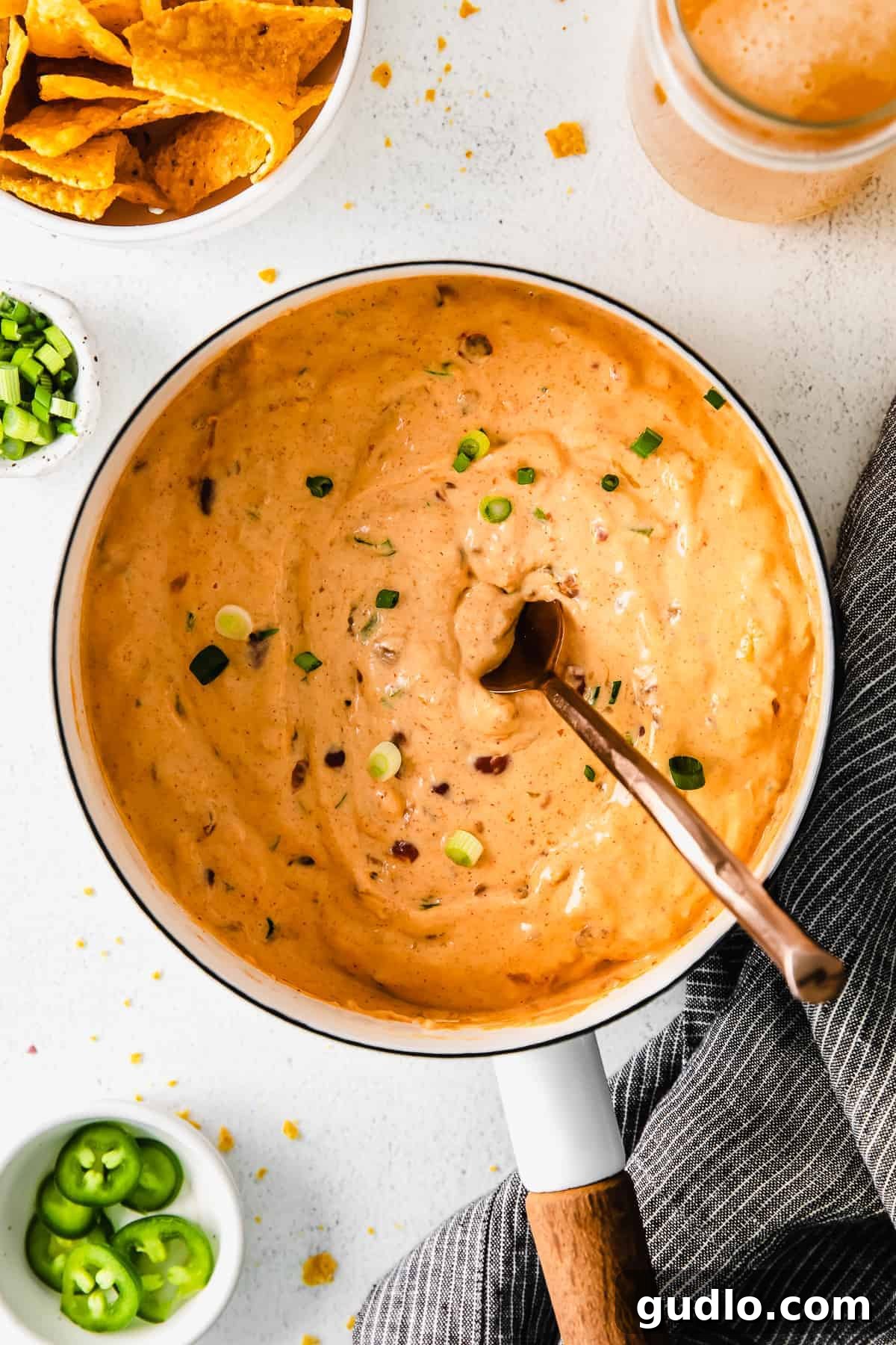 A stainless steel saucepan filled with creamy chili cheese dip, generously topped with vibrant fresh green onions, ready to be served hot.