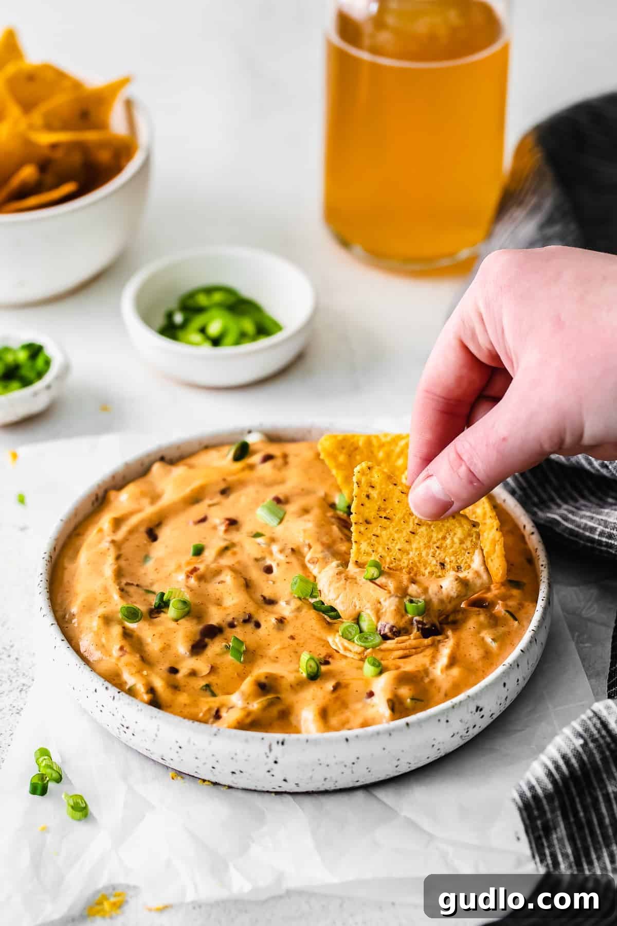 A crispy tortilla chip being dipped deeply and generously into a bowl of creamy, warm chili cheese dip, capturing the rich, gooey texture.