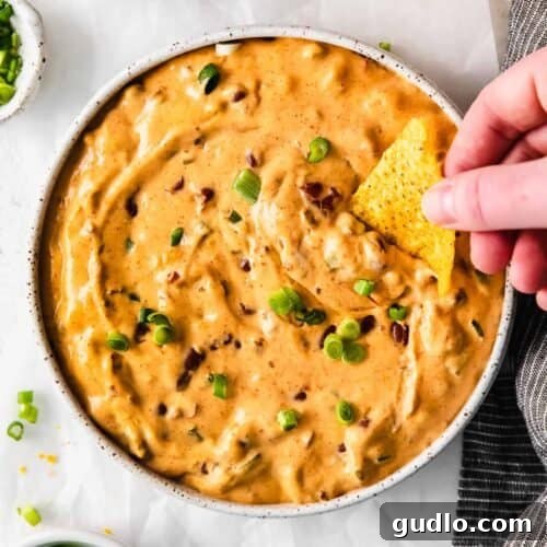 Close-up of a serving of chili cheese dip with a spoon, highlighting its creamy, rich texture and inviting warmth, garnished with green onions.
