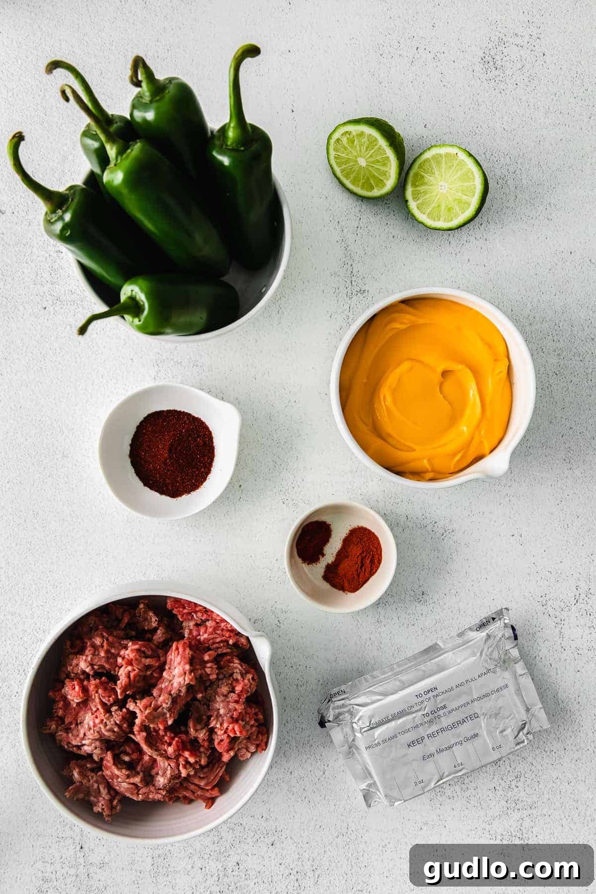 Oven-Baked Cheesy Jalapeño Dip 3 Assorted ingredients for Jalapeño Popper Dip, including cream cheese, Cheez Whiz, ground beef, and fresh jalapeños, laid out in small dishes.