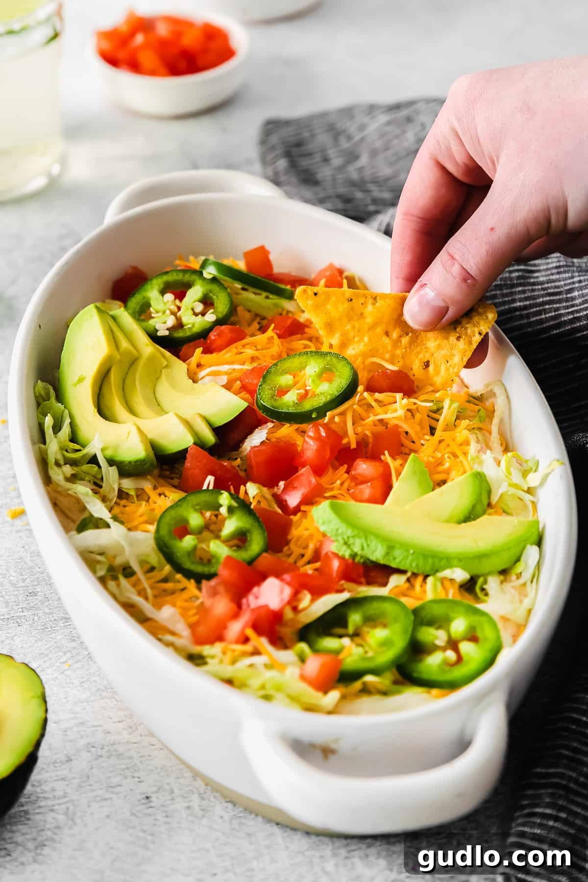A vibrant taco dip in a clear serving dish, showcasing layers of creamy dip and fresh toppings like lettuce, tomatoes, and avocado.