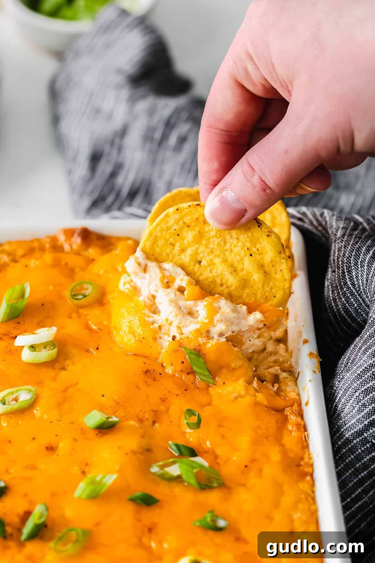 Ultimate Cheesy Crab Dip 7 A hand scooping a generous portion of hot, bubbling crab dip from a baking dish, ready to be enjoyed.