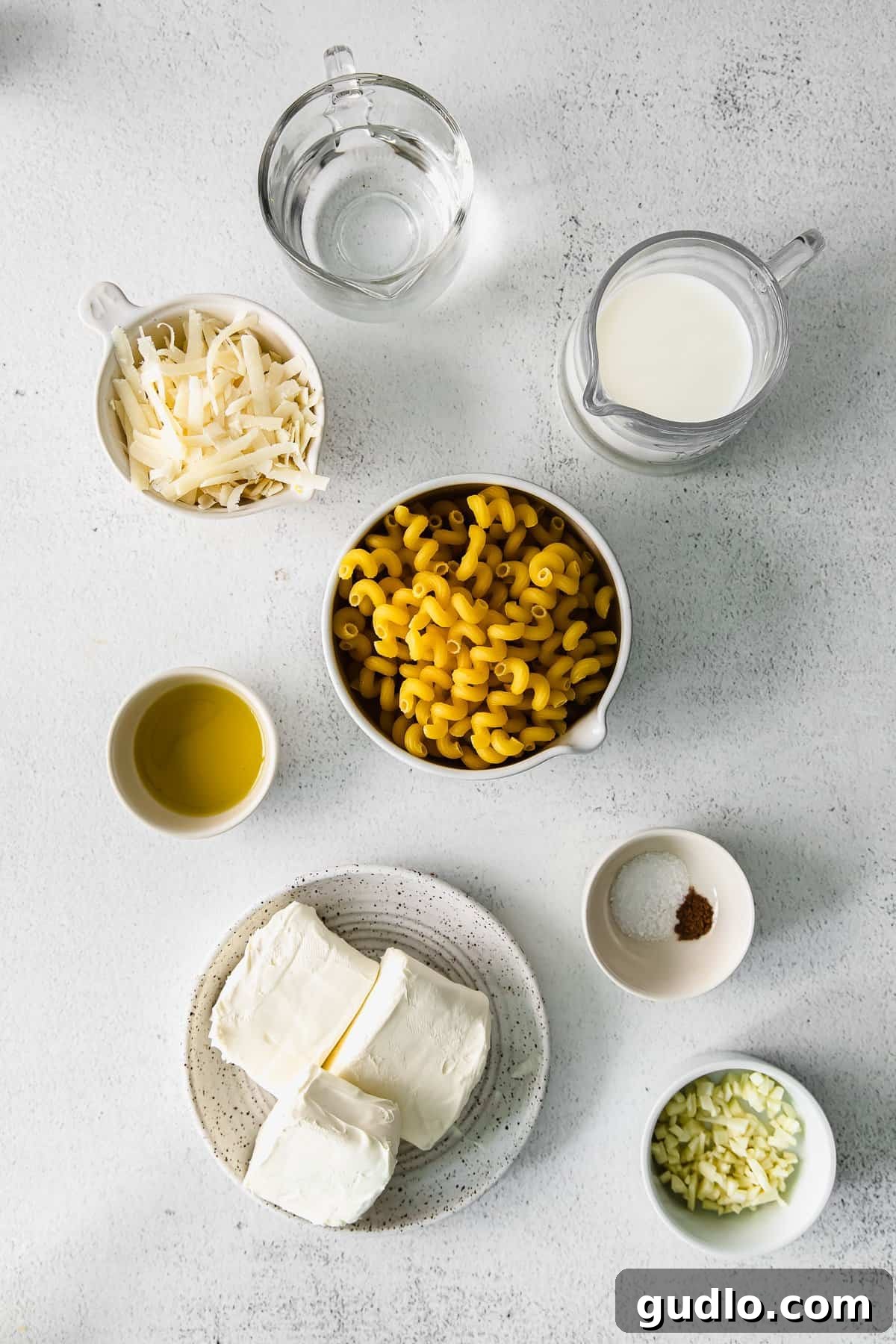 Ingredients laid out on a kitchen counter: cream cheese, milk, garlic, asiago, and spices.