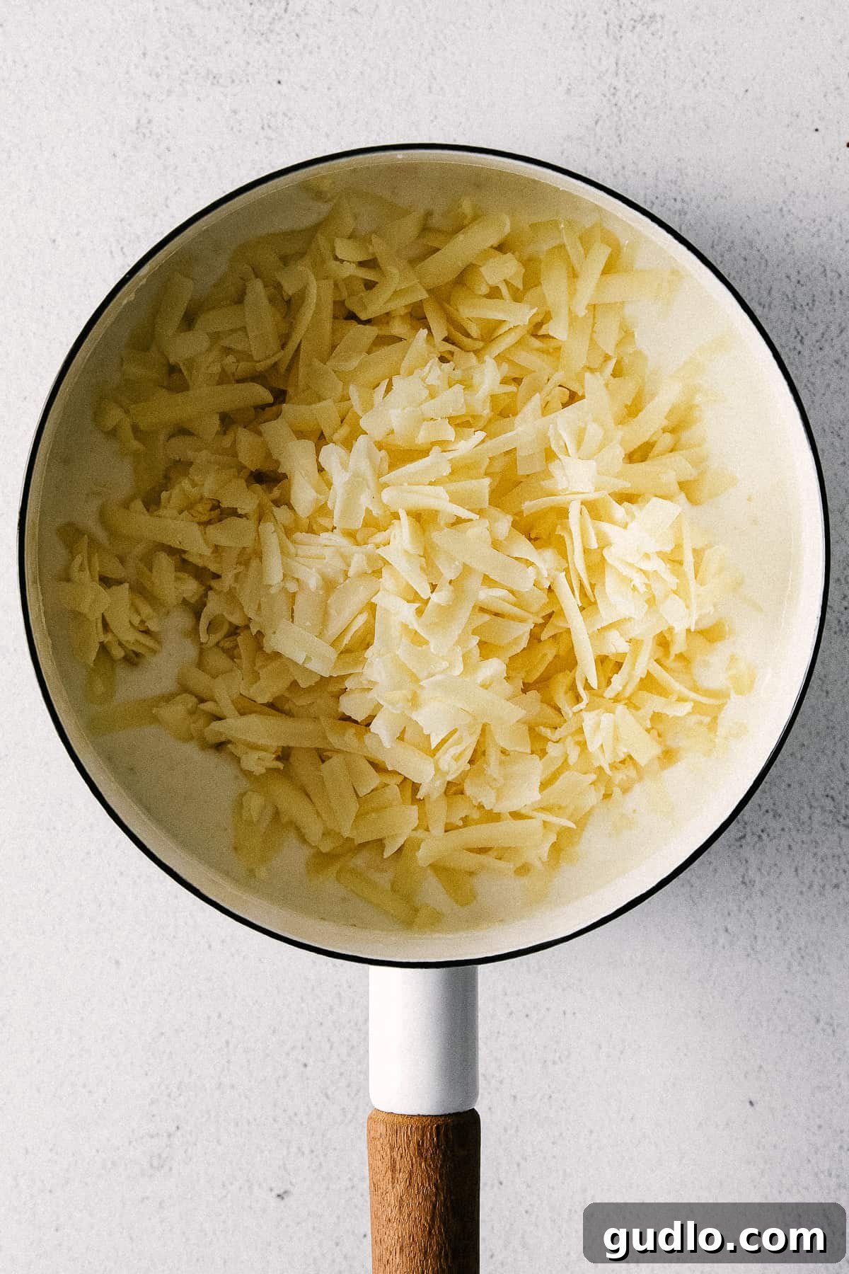 A close-up view of the rich, white cheddar cheese sauce being stirred in a pot, showing its thick, creamy consistency before adding pasta.