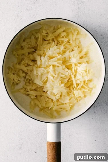 Adding shredded white cheddar cheese to the creamy sauce in a pot.