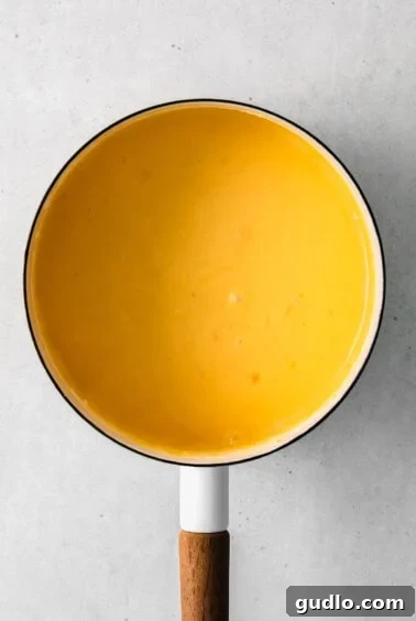 Cheese sauce simmering in a pan with a wooden spoon, indicating it's nearly ready.
