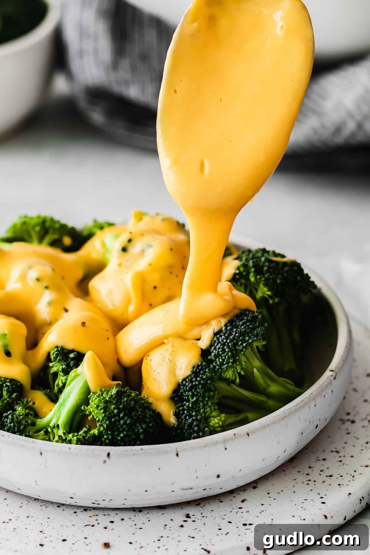 A stream of golden cheese sauce being drizzled generously over a bowl of fresh broccoli.