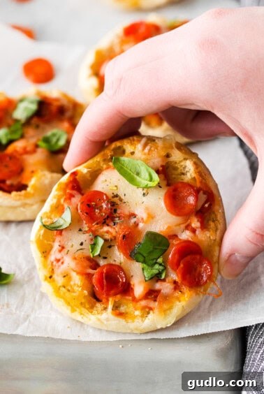 Quick English Muffin Pizzas 4 A hand presenting a finished English muffin pizza on a baking sheet, ready to eat.
