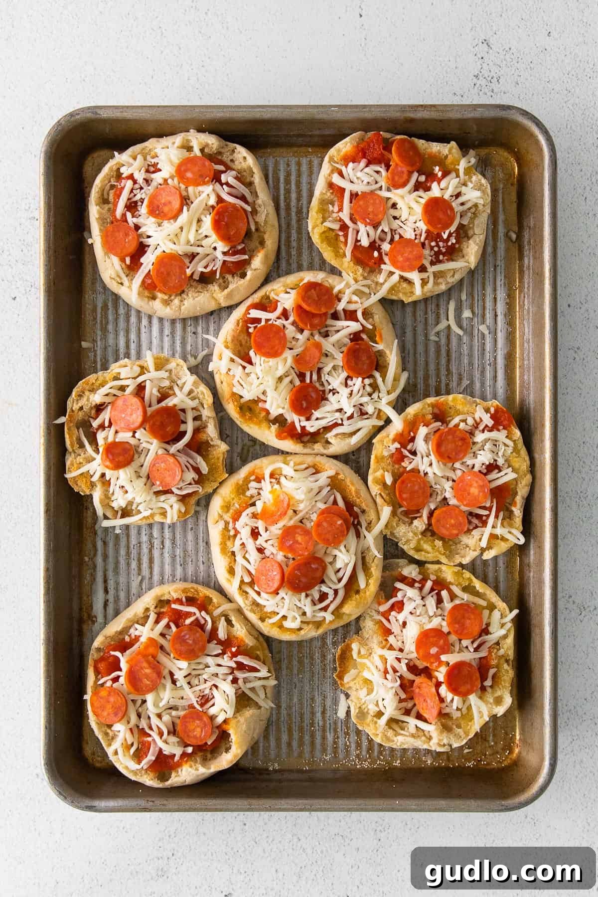 English Muffin Pizzas -- an easy 30-minute meal that the whole family will love. Top your English muffins with marinara sauce, cheese, and your favorite toppings! Multiple English muffin pizzas arranged on a baking sheet, freshly topped and ready for the oven.