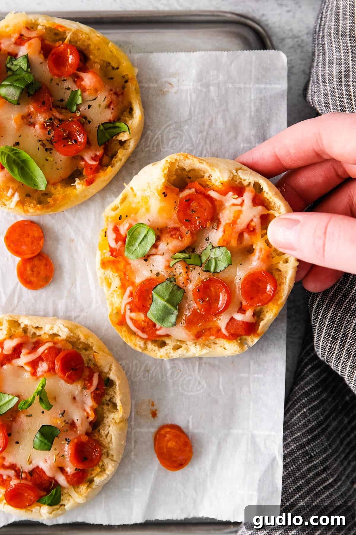 English Muffin Pizzas -- an easy 30-minute meal that the whole family will love. Top your English muffins with marinara sauce, cheese, and your favorite toppings! Close-up of a finished English muffin pizza with melted cheese, pepperoni, and fresh basil garnish.