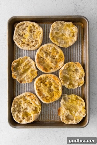 Quick English Muffin Pizzas 2 English muffin halves toasting on a baking sheet under the broiler.